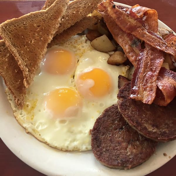 A hearty breakfast platter with three fried eggs, toast, bacon, home fries, and sausage patties.