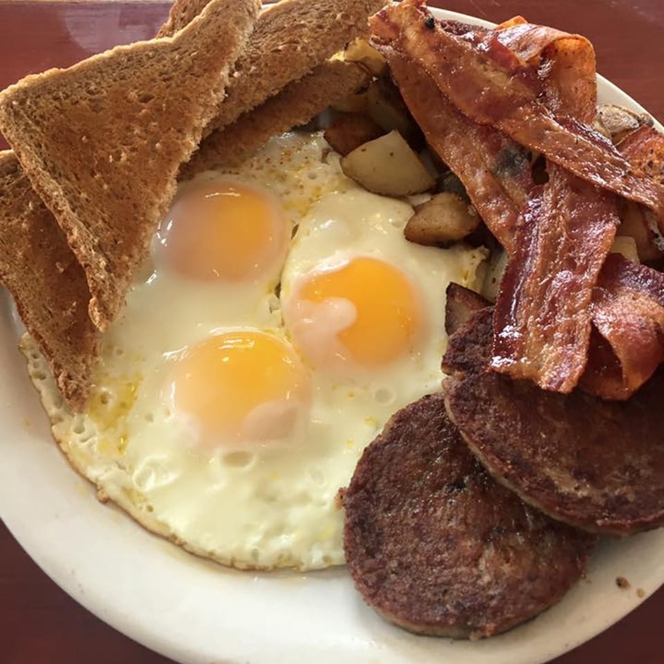 A hearty breakfast platter with three fried eggs, toast, bacon, home fries, and sausage patties.